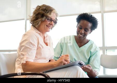 Mature woman filling out form with nurse, smiling. Stock Photo