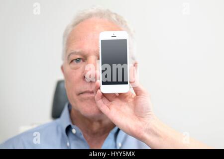 Senior man with smartphone covering eye. Stock Photo