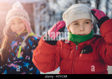 Little girl wearing read jacket putting on winter hat Stock Photo