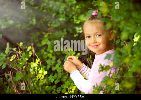 Cute little girl in a pink dress walks and plays in Palanga botanical park. Green landscaped garden in Lithuanian resort Palanga, Klaipeda County, Lit Stock Photo