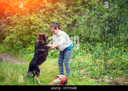 Little girl schooling dog outdoor in a forest. Girl holding a dog by the front paws. dog standing on its hind legs Stock Photo