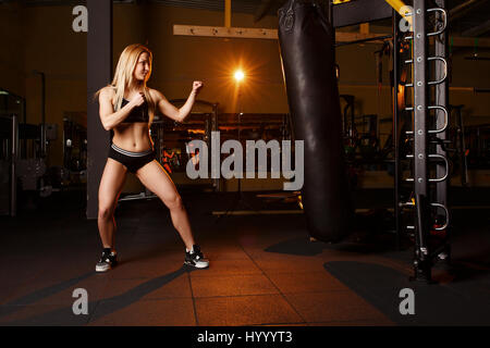 Young girl doing boxing workout in the gym. Female fighter kicking punching bag Stock Photo