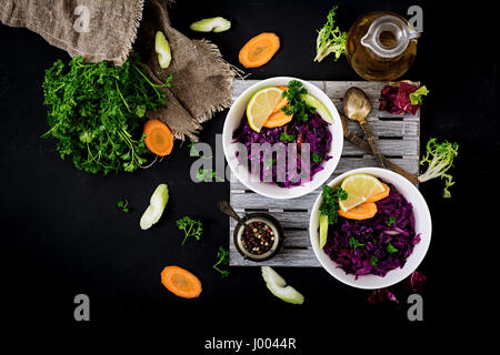 Stewed red cabbage with carrots and celery in a white bowl on a black background. Flat lay. Top view Stock Photo