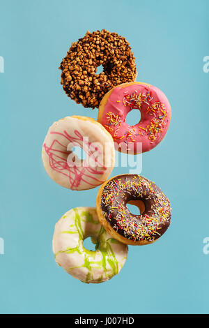 Various decorated doughnuts in motion falling on blue background. Sweet and colourful doughnuts falling or flying in motion. Stock Photo