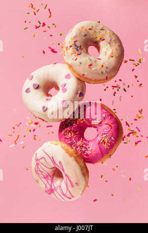 Various decorated doughnuts in motion falling on pink background. Sweet and colourful doughnuts falling or flying in motion. Stock Photo