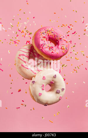 Various decorated doughnuts in motion falling on pink background. Sweet and colourful doughnuts falling or flying in motion. Stock Photo