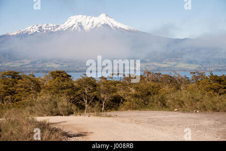 Mist rises from woodland on the shores of Lago Llanquihue, partially obscuring the snow-capped volcano of Calbuco in the Los Lagos region of Chilean P Stock Photo