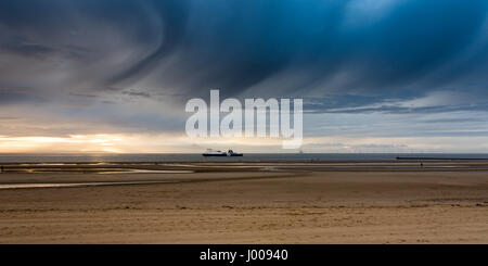 Liverpool, England, UK - November 12, 2016: A P&O ferry passes Antony Gormley's 'Another Place' sculptures on Crosby Beach, with wind farms behind. Stock Photo
