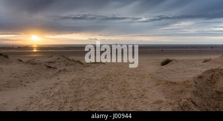 Liverpool, England, UK - November 12, 2016: The sun sets behind Antony Gormley's 'Another Place' sculptures on Crosby Beach, with wind farms behind. Stock Photo