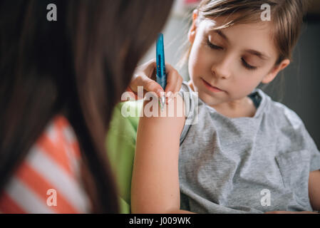 Girl writing tattoo on arm of her girlfriend with pen Stock Photo