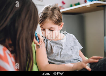 Girl writing tattoo on arm of her girlfriend with pen Stock Photo