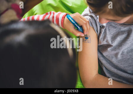 Girl writing tattoo on arm of her girlfriend with pen Stock Photo