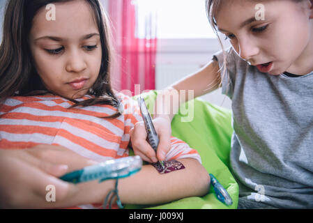 Girl writing tattoo on arm of her girlfriend with pen Stock Photo