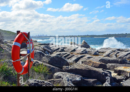 Lifesavers ring on rock platforms on rocky coastline with breaking waves and Sydney city skyline in the background, New South Wales, Australia. Stock Photo