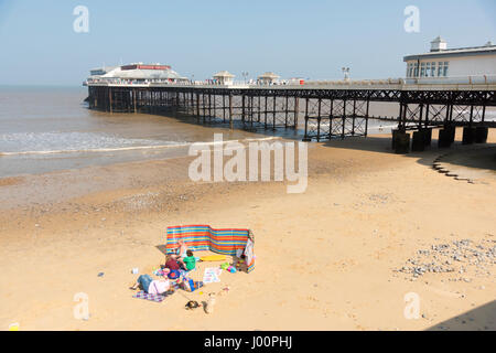 Cromer Norfolk UK 8th April 2017.  People sit on the beach by the famous pier and enjoy the glorious sunshine in warm spring weather. Temperatures rose to 19 degrees centigrade but there was a chilly wind. The fine weather is forecast to continue over the weekend. Credit Julian Eales/Alamy Live News Stock Photo