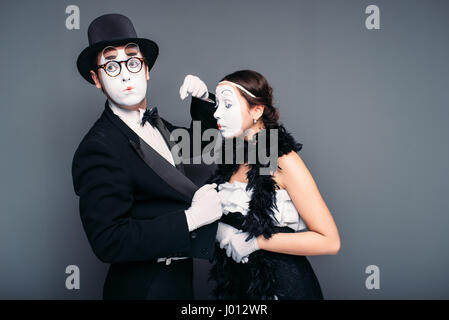 Mime artists with white makeup masks on faces. Pantomime theater actor and actress performing against black background. Comedy performers Stock Photo