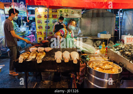 Chiang Mai, Thailand - August 27, 2016:  Thai woman cooks grilled fish at the Saturday Night Market on August 27, 2016 in Chiang Mai, Thailand. Stock Photo