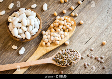 Assorted Legumes (chickpeas, green lentils, white beans) over rustic wooden background - ingredient for healthy vegan, vegetarian, diet food meal, veg Stock Photo