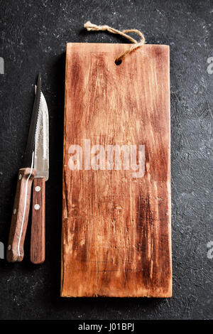 Rustic wooden cutting board and knives on black stone background close up - rustic empty copy space for text, design element Stock Photo