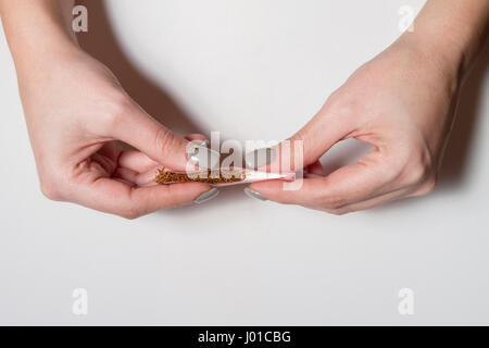 Hands of a woman rolling a cigarette with rolling tobacco on clear background. Soft focus. Stock Photo