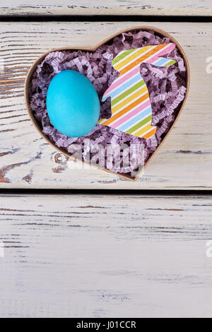 Easter gift box, wooden surface. Blue egg in shredded paper. Stock Photo