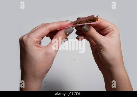 Hands of a woman rolling a cigarette with rolling tobacco on clear background. Soft focus. Stock Photo