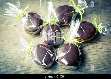 chocholate and gingerbread easter eggs in plastic bags and green ribbon on old wooden table or floor Stock Photo