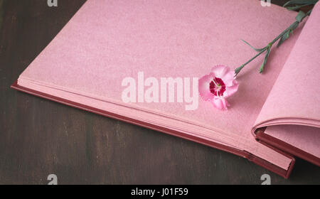 Opened vintage photo album with pink pages on wooden table, sweet william flowers, space for romantic text, selective focus Stock Photo