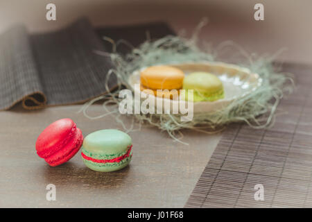 Traditional french macaroons, two on the table and two on the plate behind. Selective focus, vignette, pastel color filter used Stock Photo