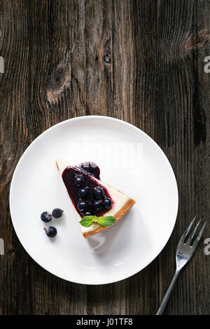 Slice of cheesecake with blueberry and black currant on white plate over wooden background. Top view with copy space for your text Stock Photo