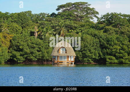 Tropical bungalow overwater with thatched palm roof and lush green vegetation on the sea shore, Bocas del Toro, Caribbean, Central America, Panama Stock Photo