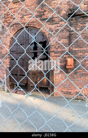 Rusty door of a brick building behind fence Stock Photo