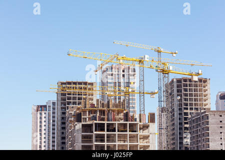construction site with high-rise unfinished apartment building and yellow cranes on sky background Stock Photo