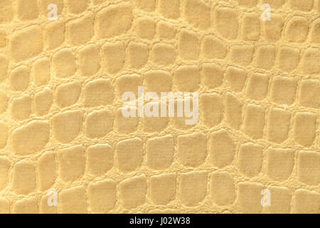 Light yellow background from a soft upholstery textile material, closeup. Golden fabric with pattern imitating crocodile skin.. Textured backdrop. Stock Photo