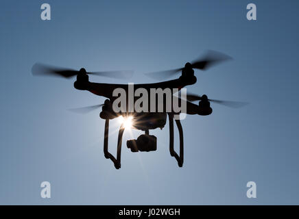 Quadcopter drone flying in front of the sun with backlight, closeup Stock Photo