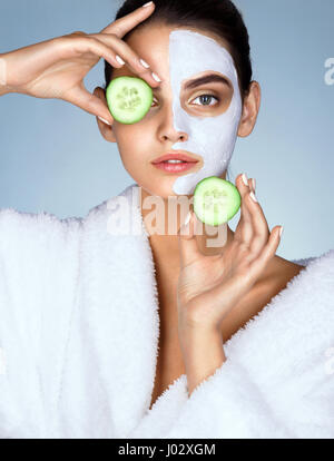 Attractive girl holding cucumber slices up to her eyes. Photo of girl with moisturizing facial mask. Beauty & Skin care concept Stock Photo