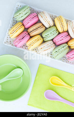 assortment of candy colored macaroons arrange  in a pretty tray with a lime green napkin and colored spoons and a small dish. The image is vertical an Stock Photo
