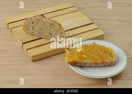Orange marmalade on piece of toast and remaining nine gain loaf on wooden cutting board Stock Photo