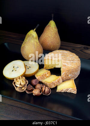 Soft washed-rind cheese, walnut, hazelnuts and pears on the black plate Stock Photo