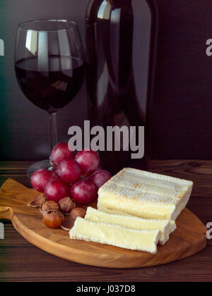 Brick shaped cheese with white mold, hazelnuts, red grape and wine in the glass and bottle