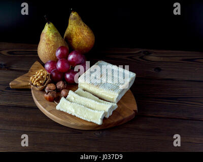Brick shaped cheese with white mold, hazelnuts, walnut, red grape and pears on the textured wooden board