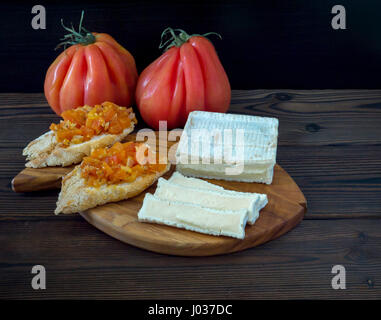 Brick shaped white mold cheese, ripe tomatoes and toasts on the textured wooden board
