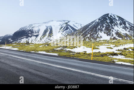 Icelandic landscape with highway, green moss growing on rocks and snowy mountains on horizon, South coast of Iceland Stock Photo