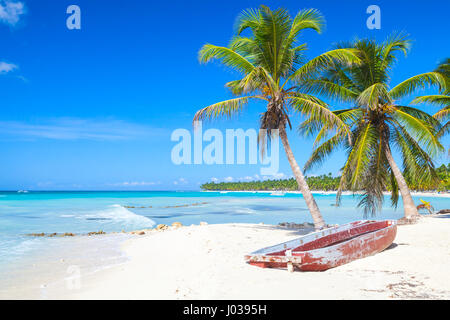 Coconut palms and old red pleasure boat are on white sandy beach. Caribbean Sea, Dominican republic landscape, Saona island coast, touristic resort Stock Photo