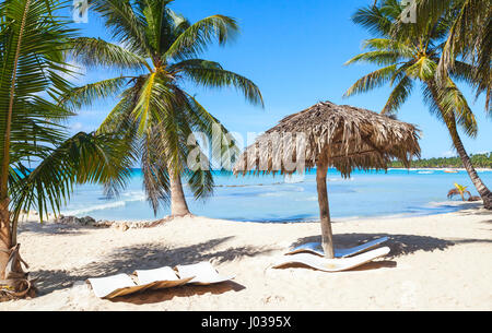 Coconut palms, empty loungers and umbrella are on white sandy beach. Caribbean Sea, Dominican republic, Saona island coast, popular touristic resort Stock Photo