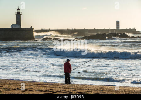 Man fishing from the beach in Foz do Douro district of Porto city, second largest city in Portugal. View with Felgueiras Lighthouse Stock Photo