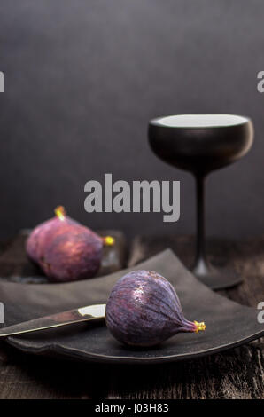 Figs, unusual spoon, square black plate and cocktail glass on black background Stock Photo