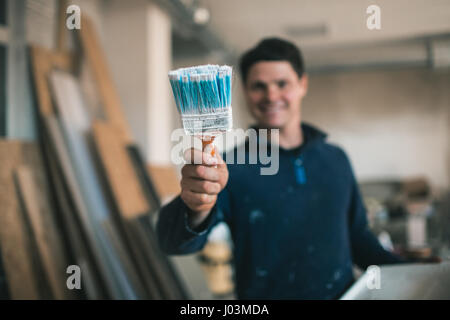 The painter in working clothes paints an imaginary wall. Focus on the brush Stock Photo