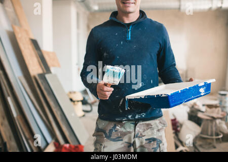 The painter in working clothes paints an imaginary wall. Focus on the brush Stock Photo