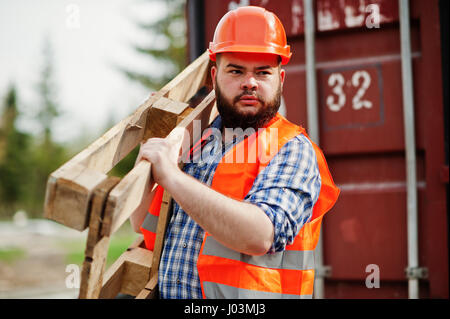 Brutal beard worker man suit construction worker in safety orange helmet with pallet. Stock Photo